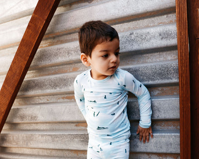 Child wearing a light blue pajama set with a pattern, standing in front of a wooden and metal wall.